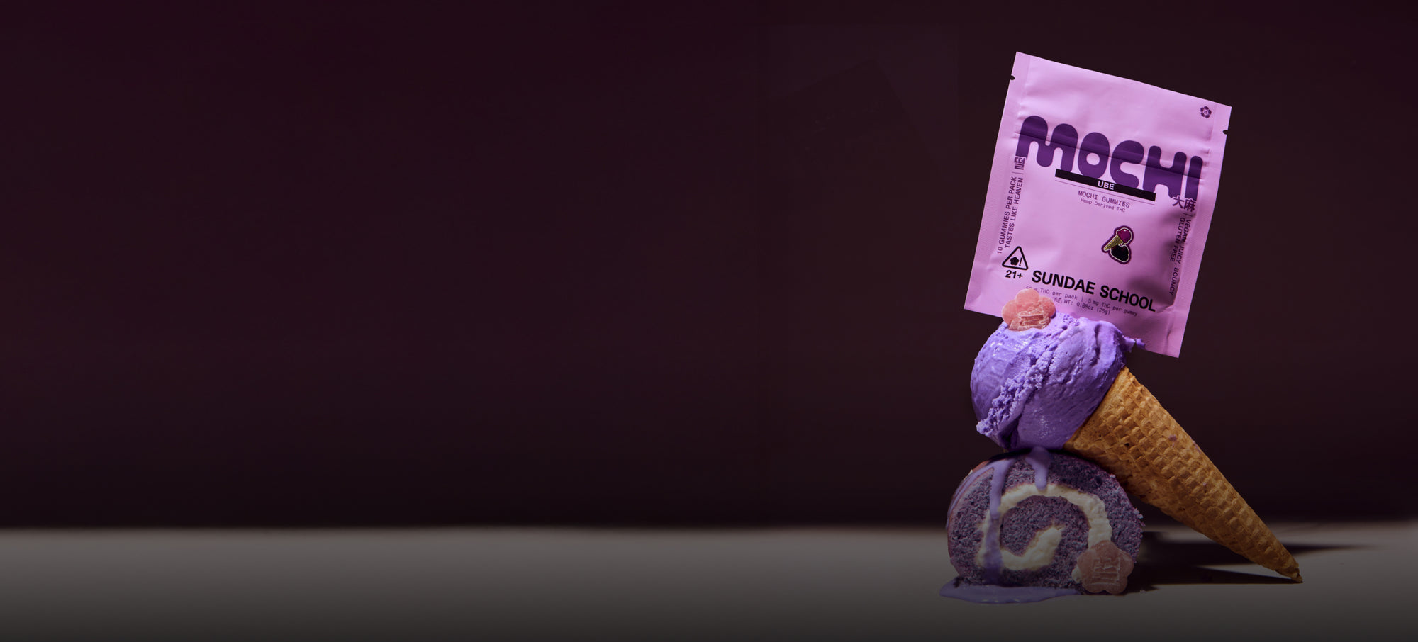 Sundae School 5mg 10-pack Ube mochi and its packaging stacked on top of melting ube ice cream on a cone stacked on a ube roll cake against a dark purple background.
