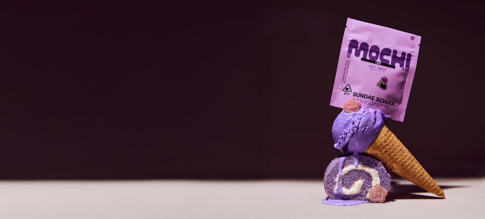 Sundae School 5mg 10-pack Ube mochi and its packaging stacked on top of melting ube ice cream on a cone stacked on a ube roll cake against a dark purple background.