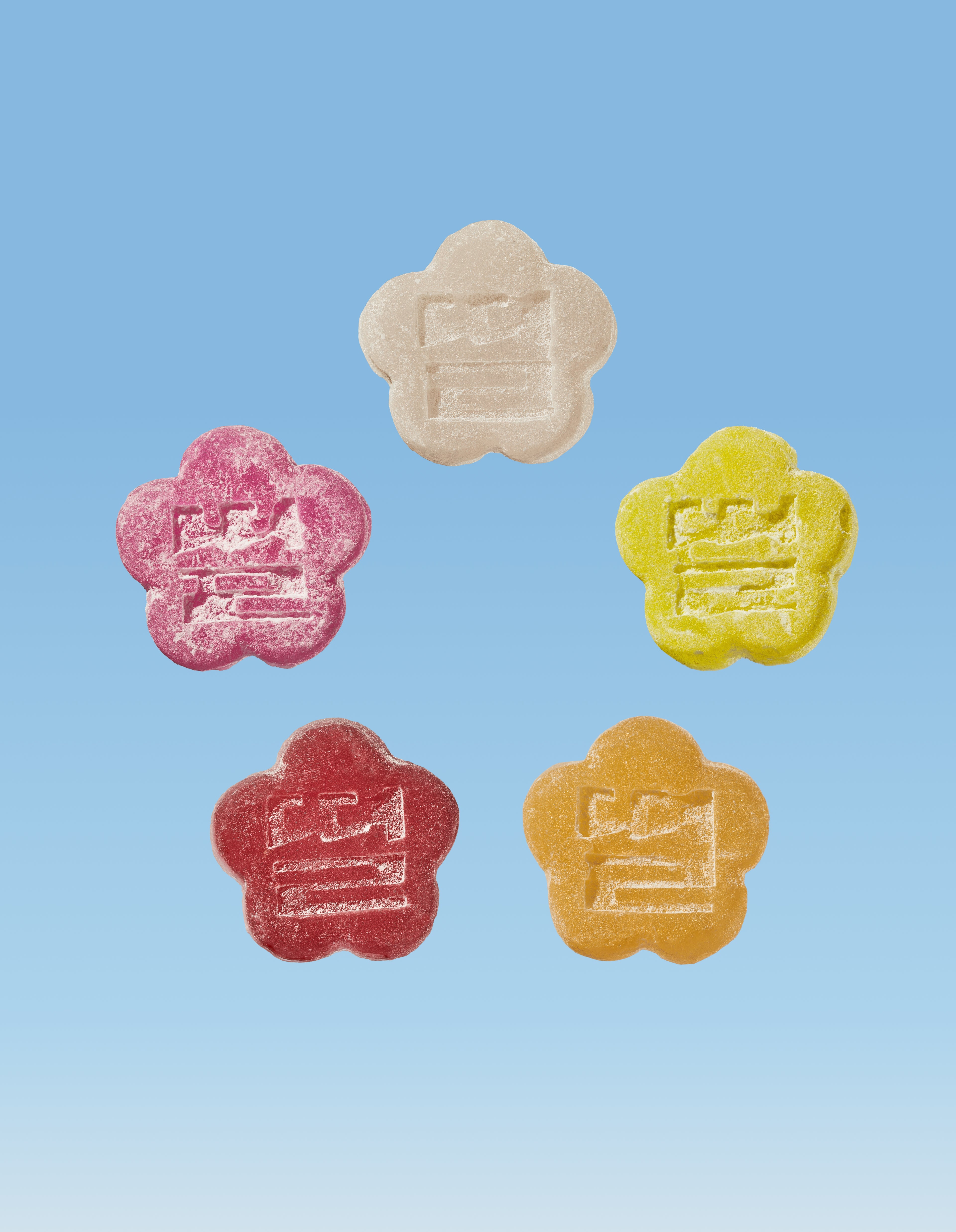 Five colorful  flower-shaped Mochi Gummies in Red, White, Yellow,  Dark Pink and Bright Pink on a blue background