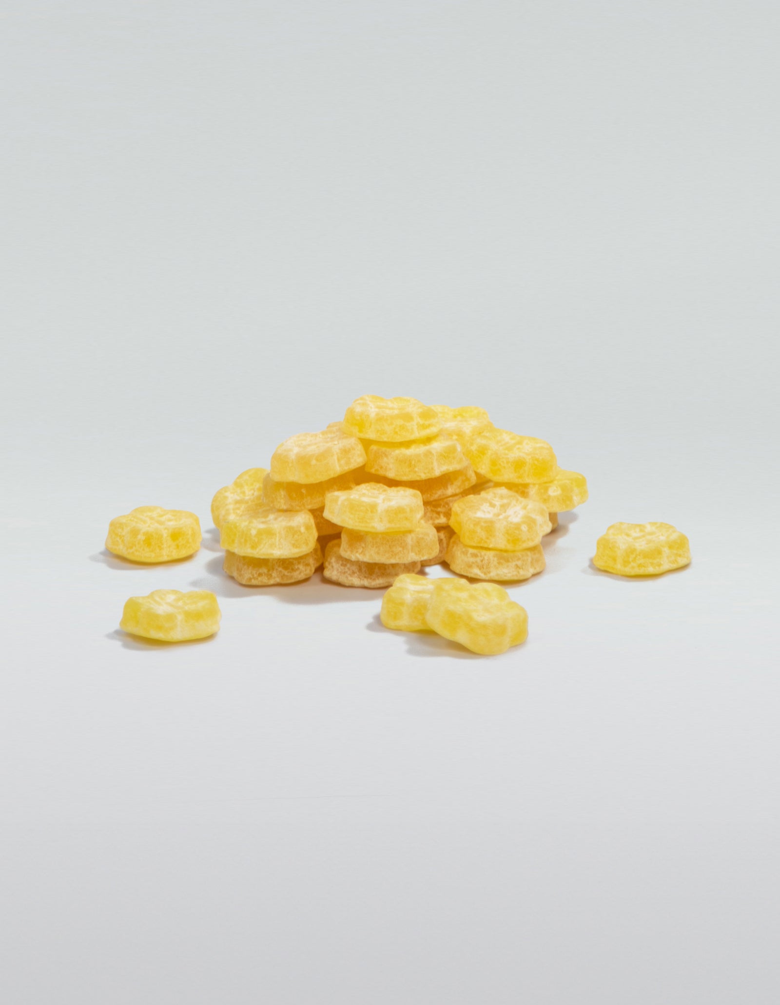 A image of a pile of Sour Yuzu, yellow, gummies stacked and scattered on a white surface. 