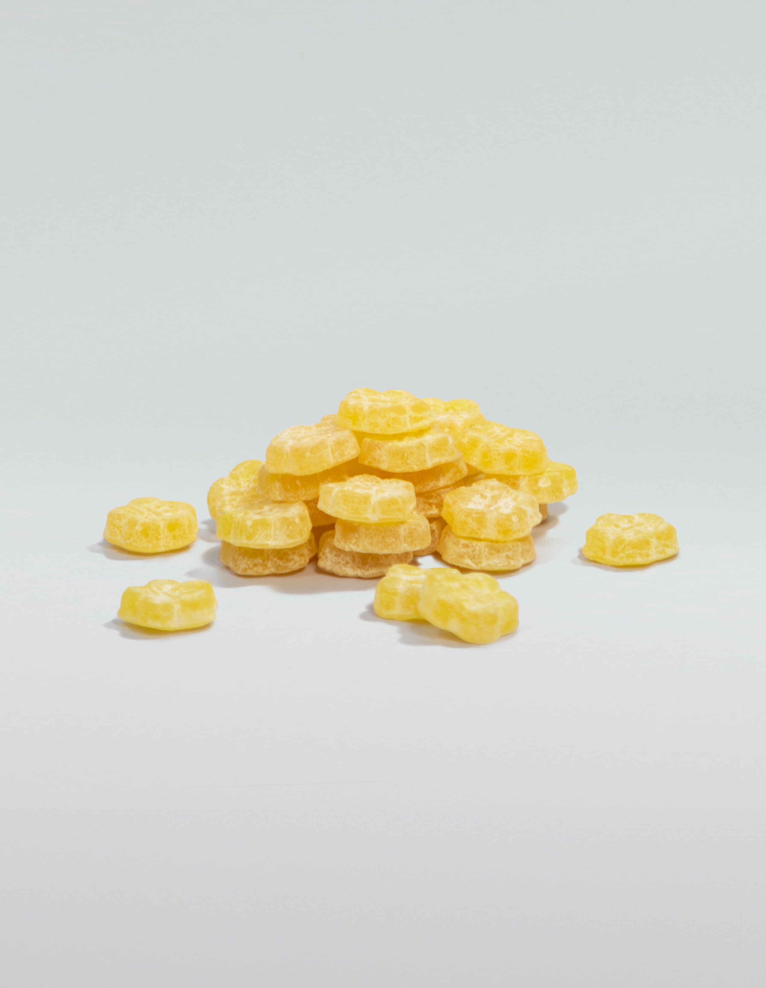 A image of a pile of Sour Yuzu, yellow, gummies stacked and scattered on a white surface. 