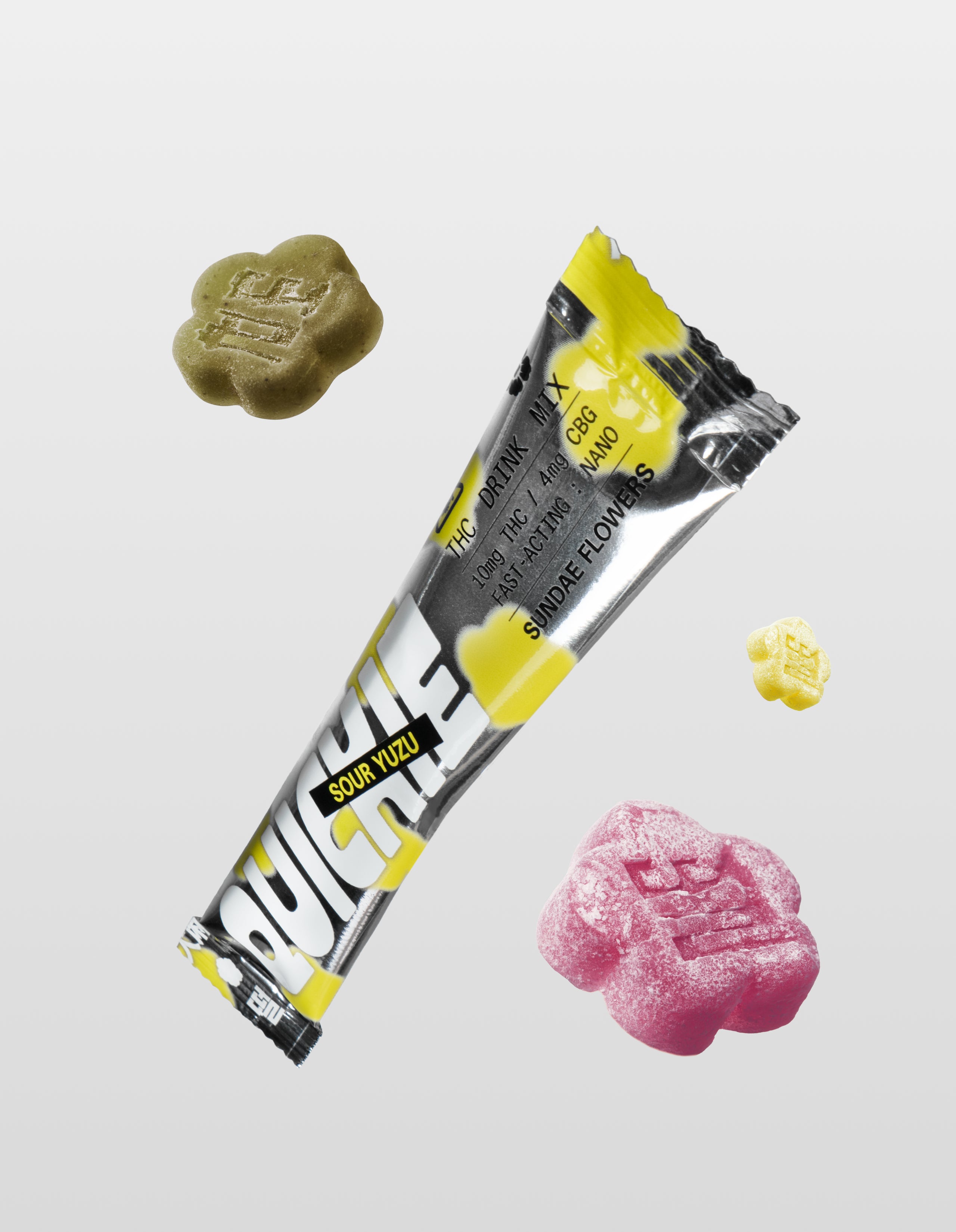 A Sour Yuzu Quickie drink mix packet floating diagonally, surrounded by three flower-shaped mochi gummies in green, yellow, and pink, showcasing the different flavors.