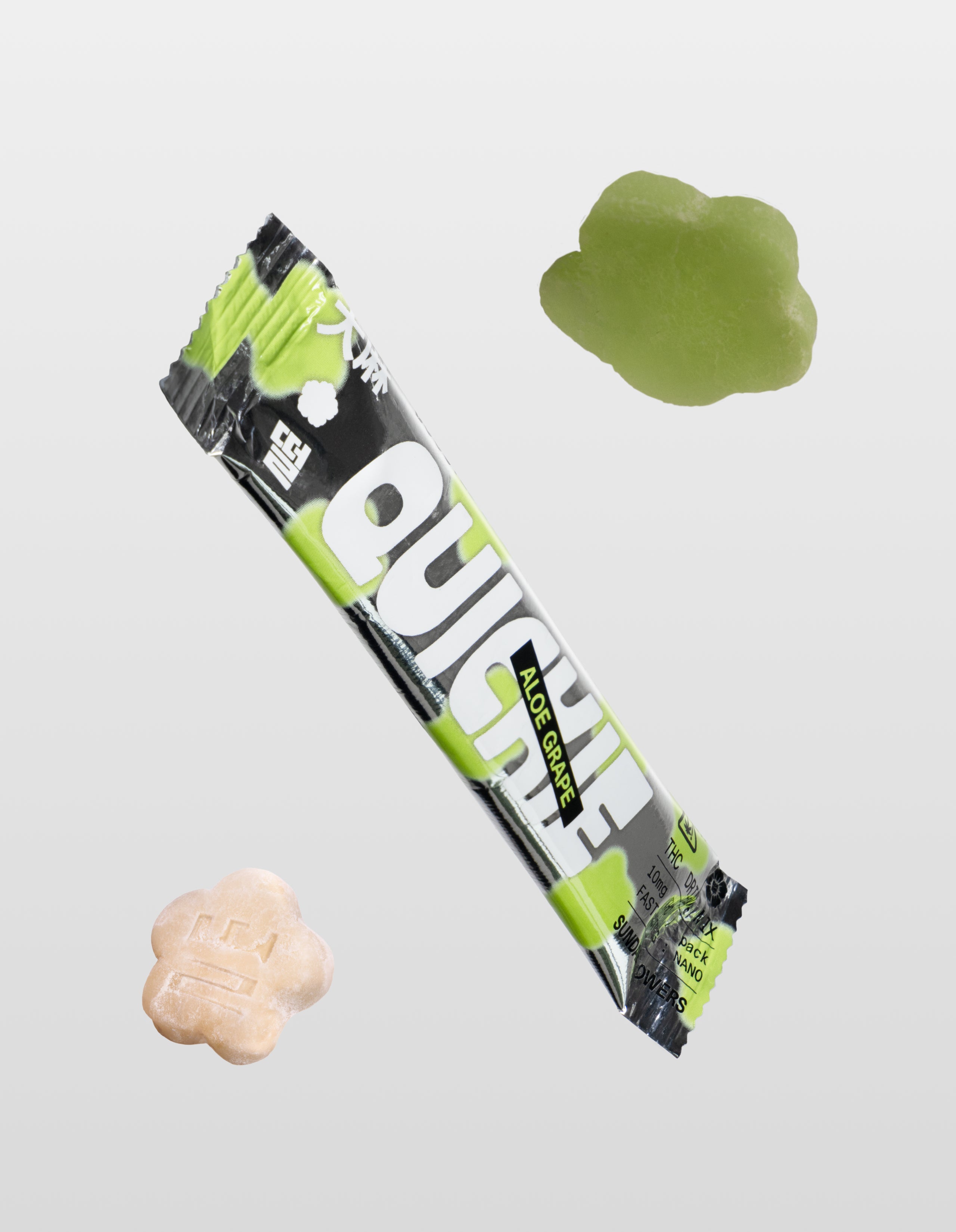 A single Aloe Grape Quickie drink mix packet floating diagonally between two flower-shaped mochi gummies—one translucent green and one creamy white—set against a minimal gray gradient.