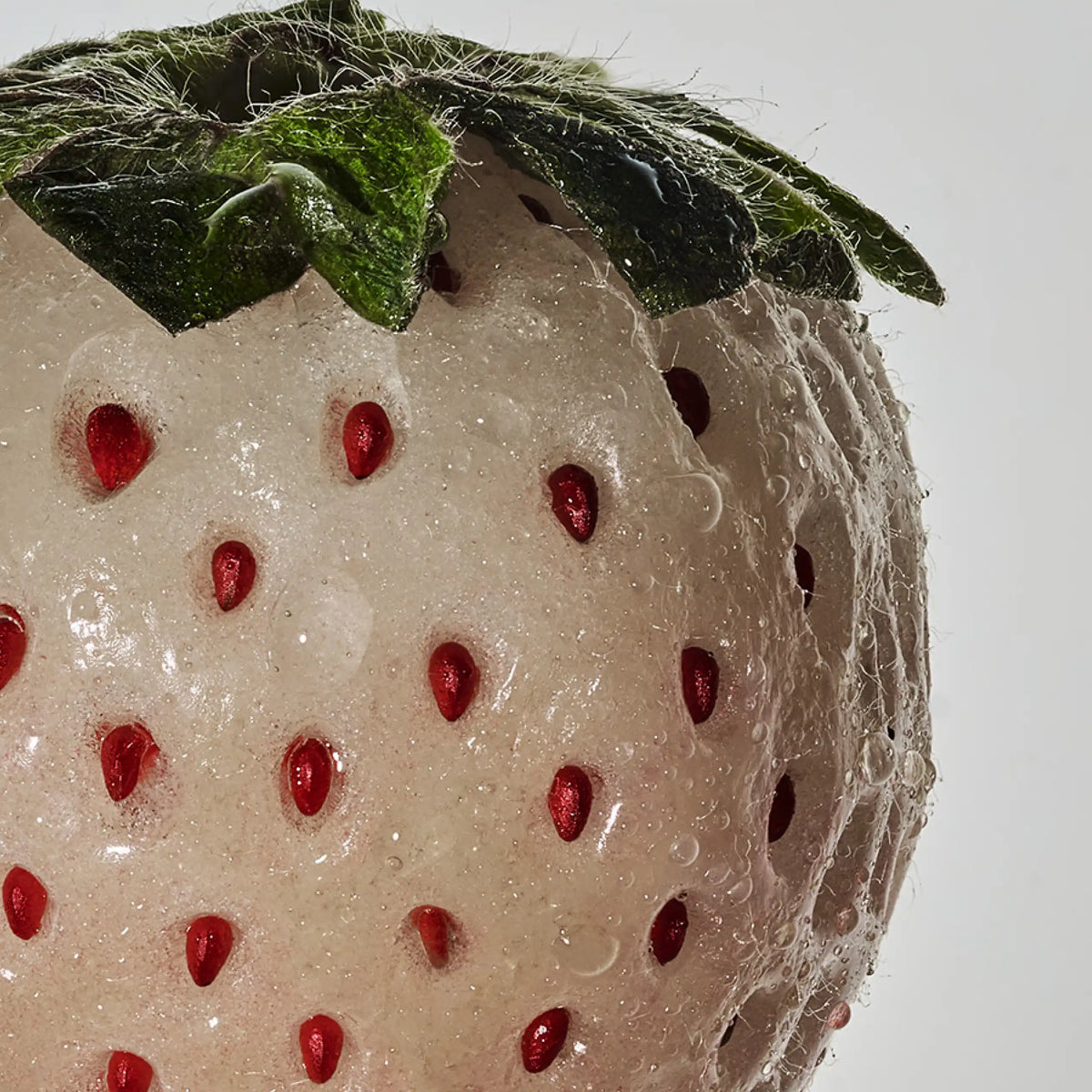A macro shot of a white strawberry with red seeds and water droplets on the fruit