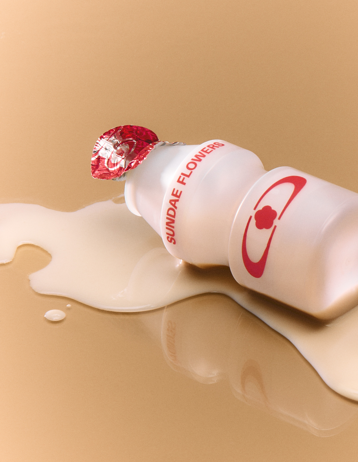 Plastic yogurt drink bottle labelled "Sundae Flowers" laid on  yellow reflective floor, on top of the spilled drink.