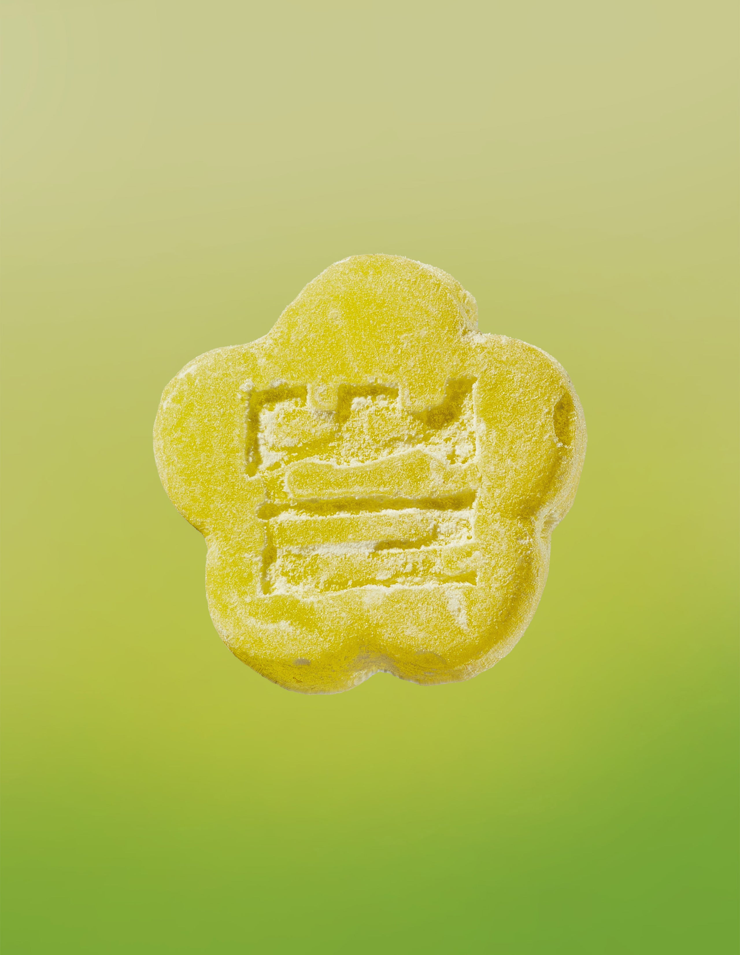 An image of a Sour Yuzu gummy on a gradient background going yellow to lime green. 