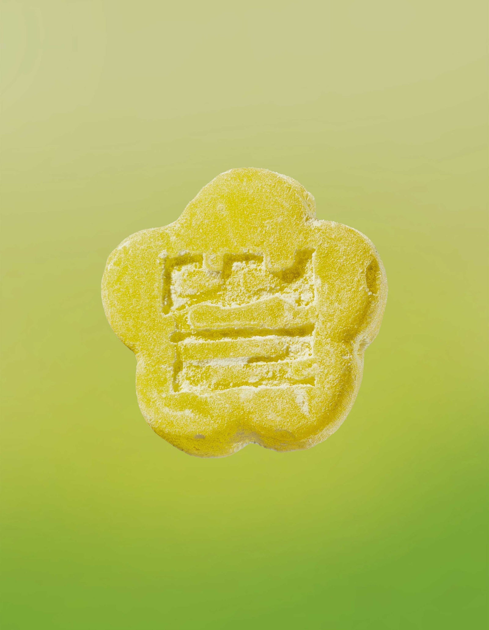 Image of a Sour Yuzu gummy on a gradient background going yellow to lime green. 
