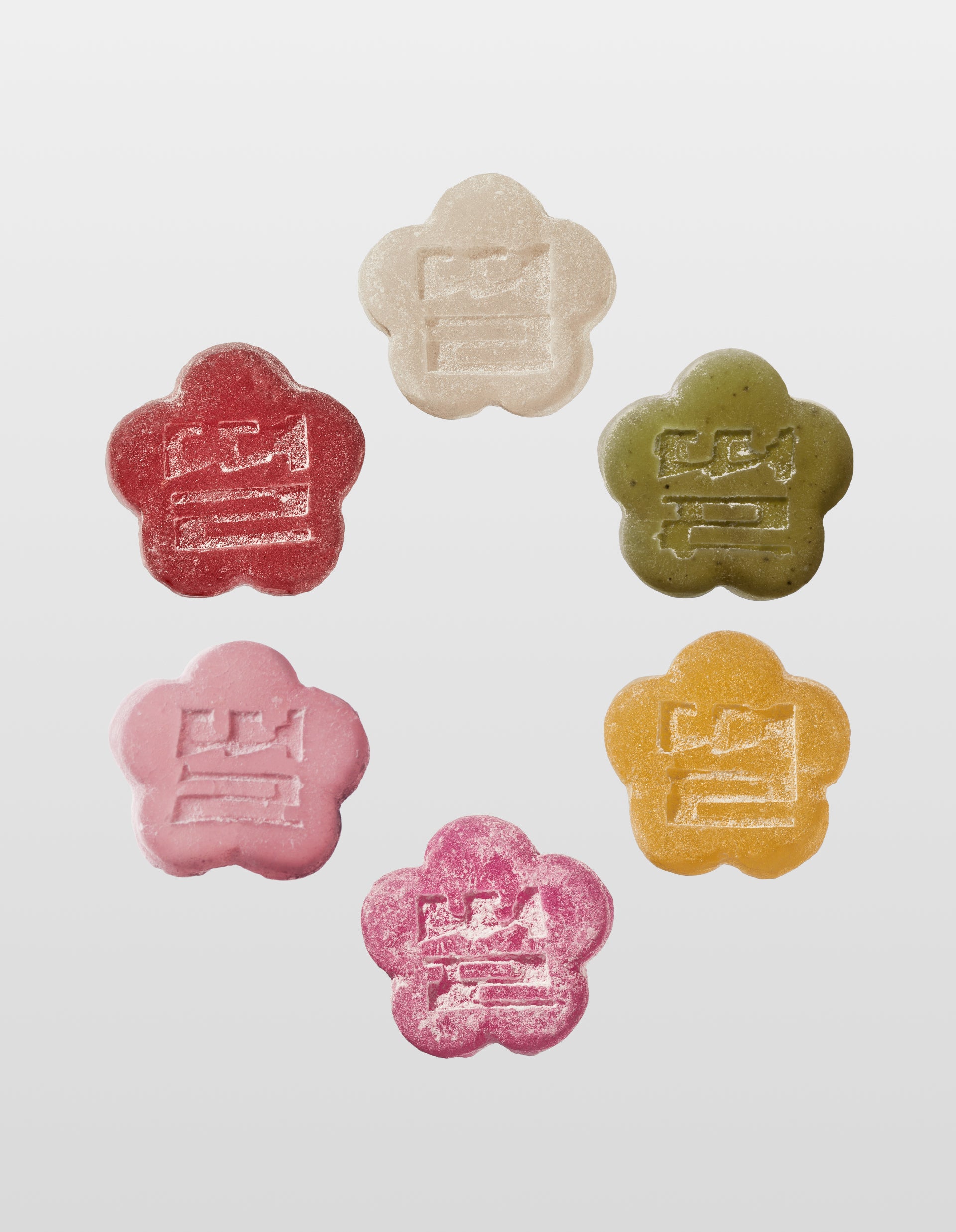 Six colorful  flower-shaped Mochi Gummies in Red, White, Green, Yellow,  Dark Pink and Bright Pink on a white background