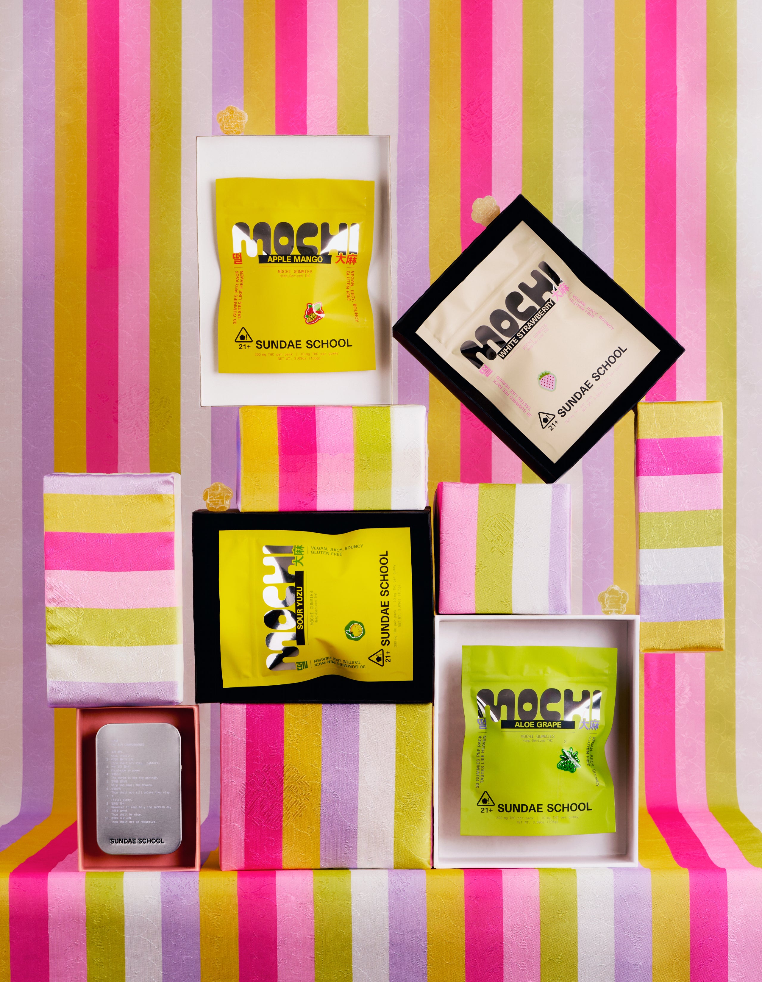 An Image of 30ct Apple Mango Mochi gummy, Sour Yuzu Mochi gummy, Aloe Grape Mochi gummy,  White Strawberry Mochi Gummy packagings in a resealable bag form individually put in a box along with Mochi gummies, Sundae School Mochi Tin, and Sundae School Bojagi. 