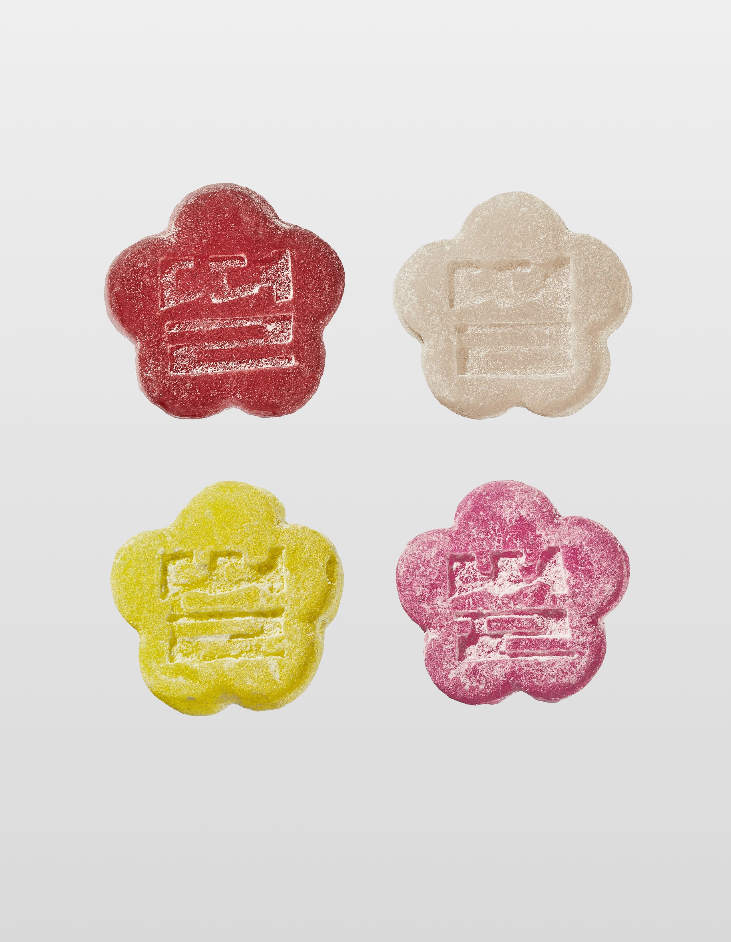 Four colorful  flower-shaped Mochi Gummies in Wine Red, White, Yellow and Pink on a white background