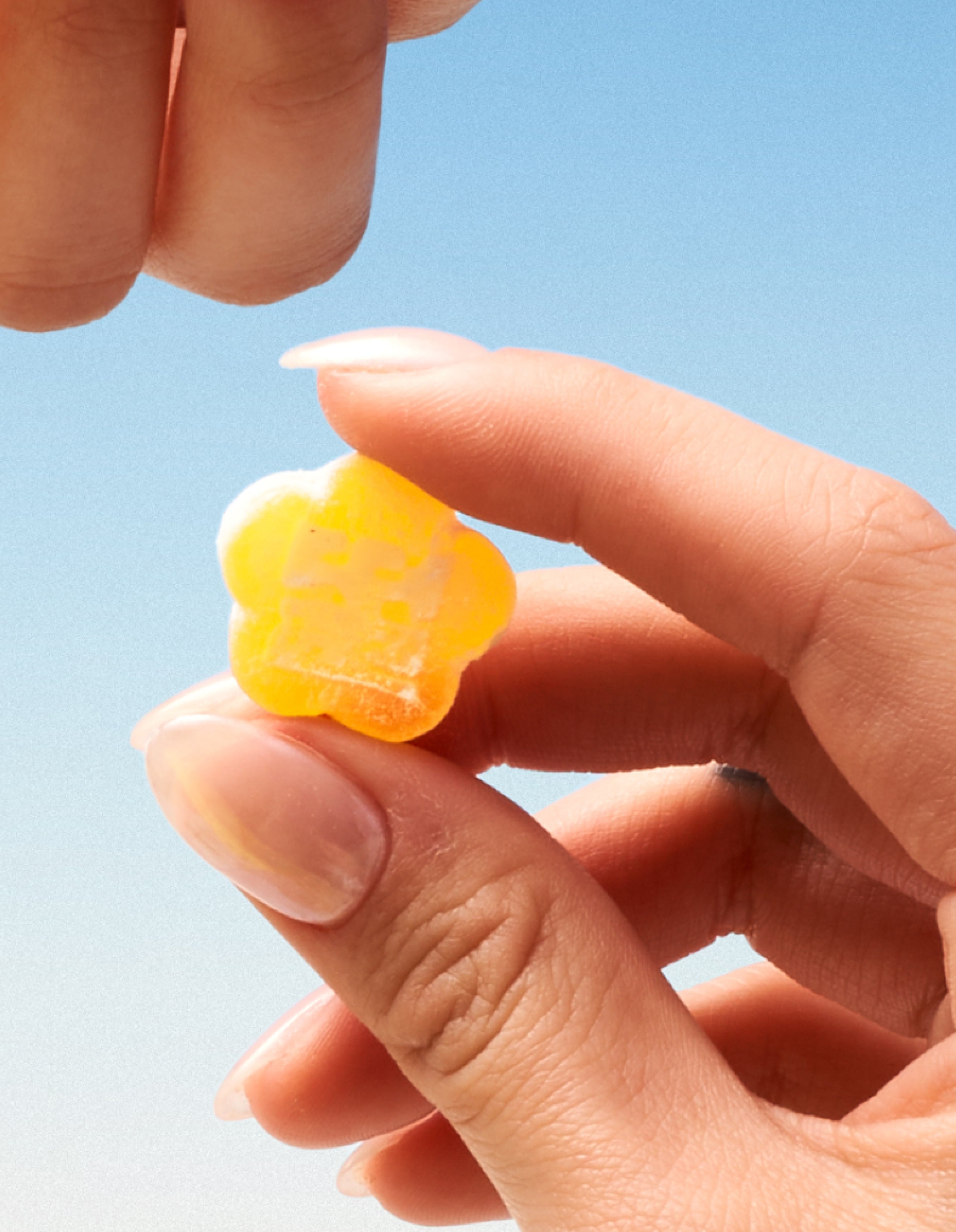 Hand holding Sundae School Sour Yuzu mochi gummy against blue sky background