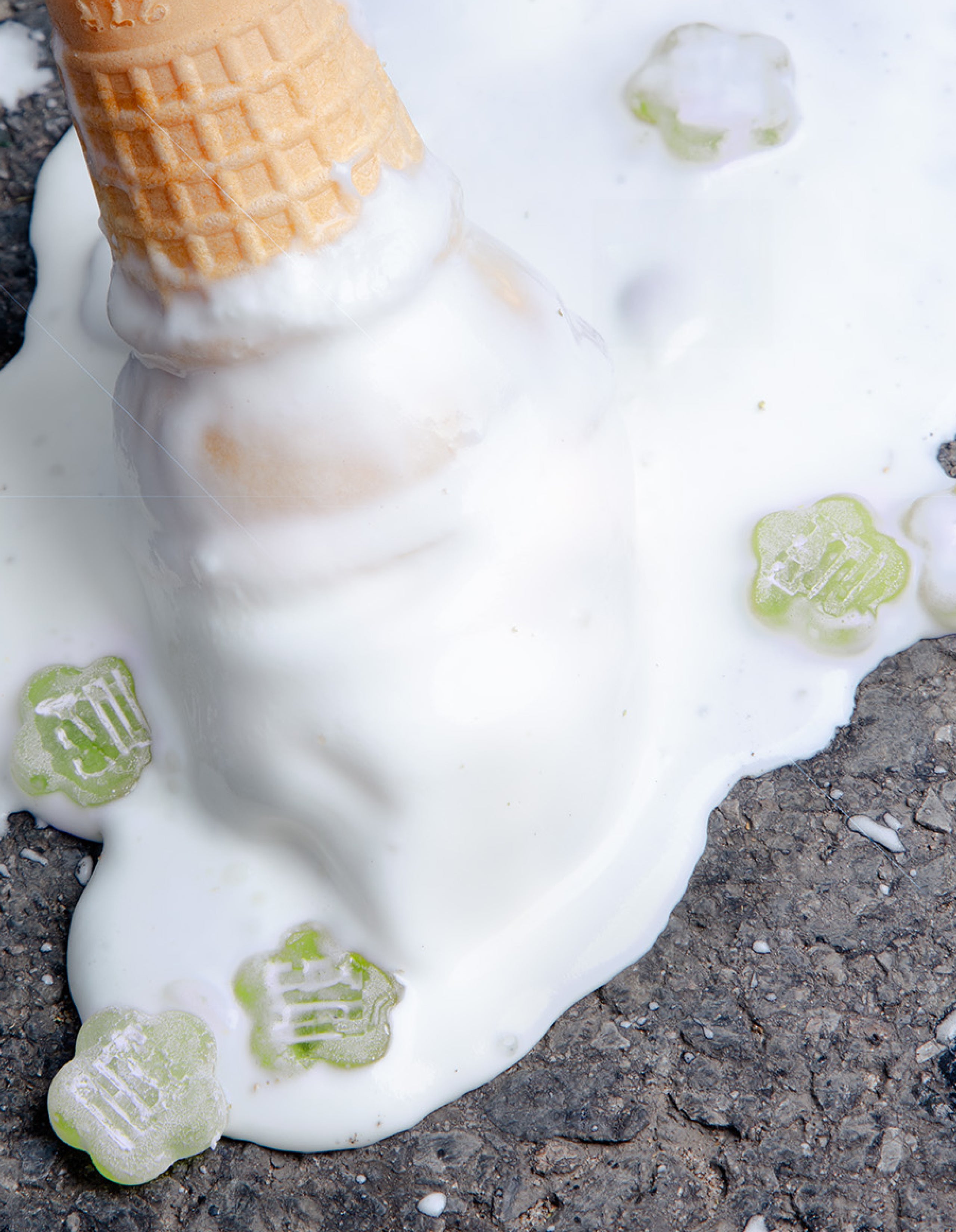 Melted ice cream cone with Sundae School Aloe Grape mochi gummies embedded in surface on concrete ground
