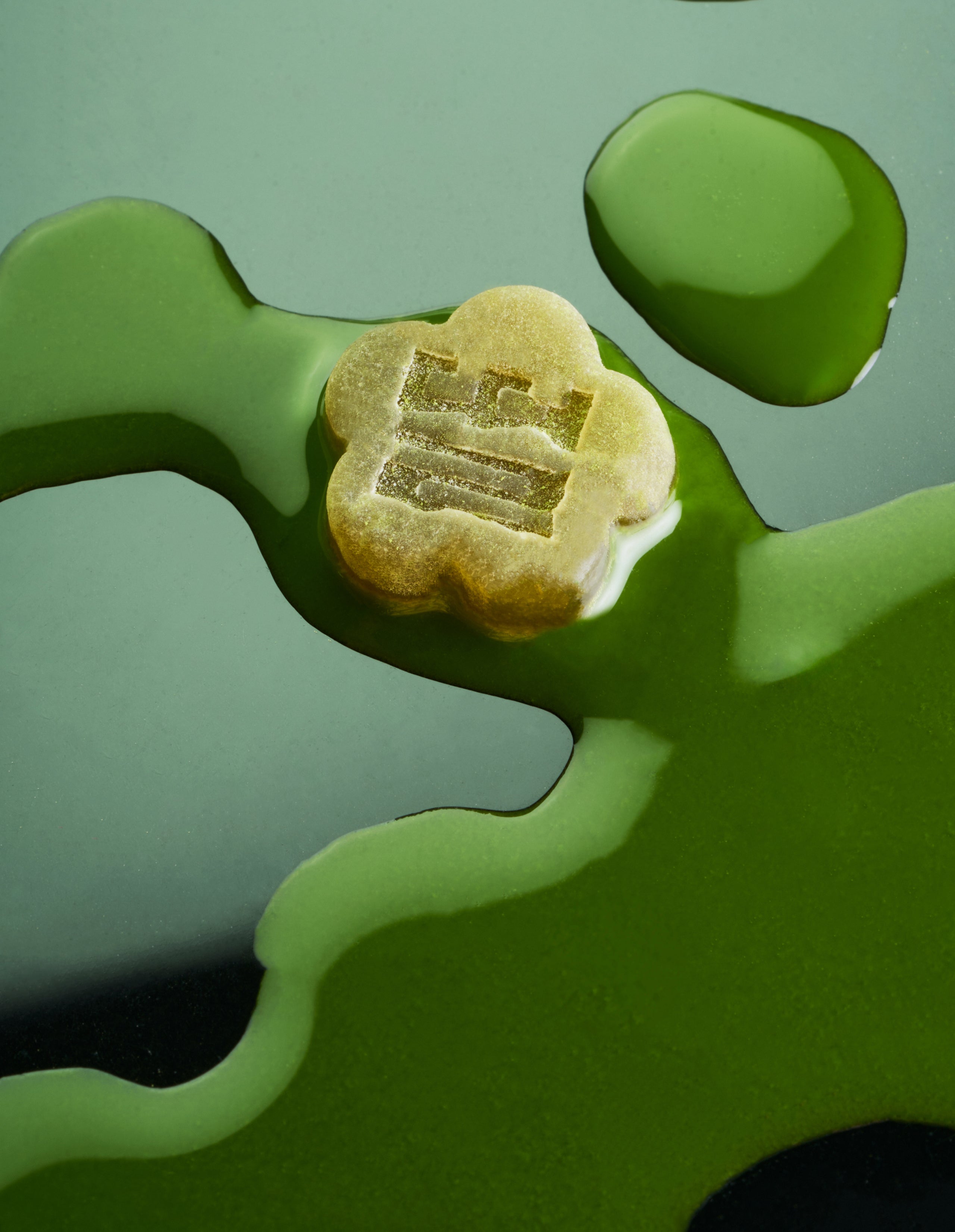 Sundae School Matcha flower-shaped mochi gummy laying in a drizzle of matcha latte in artistic styling