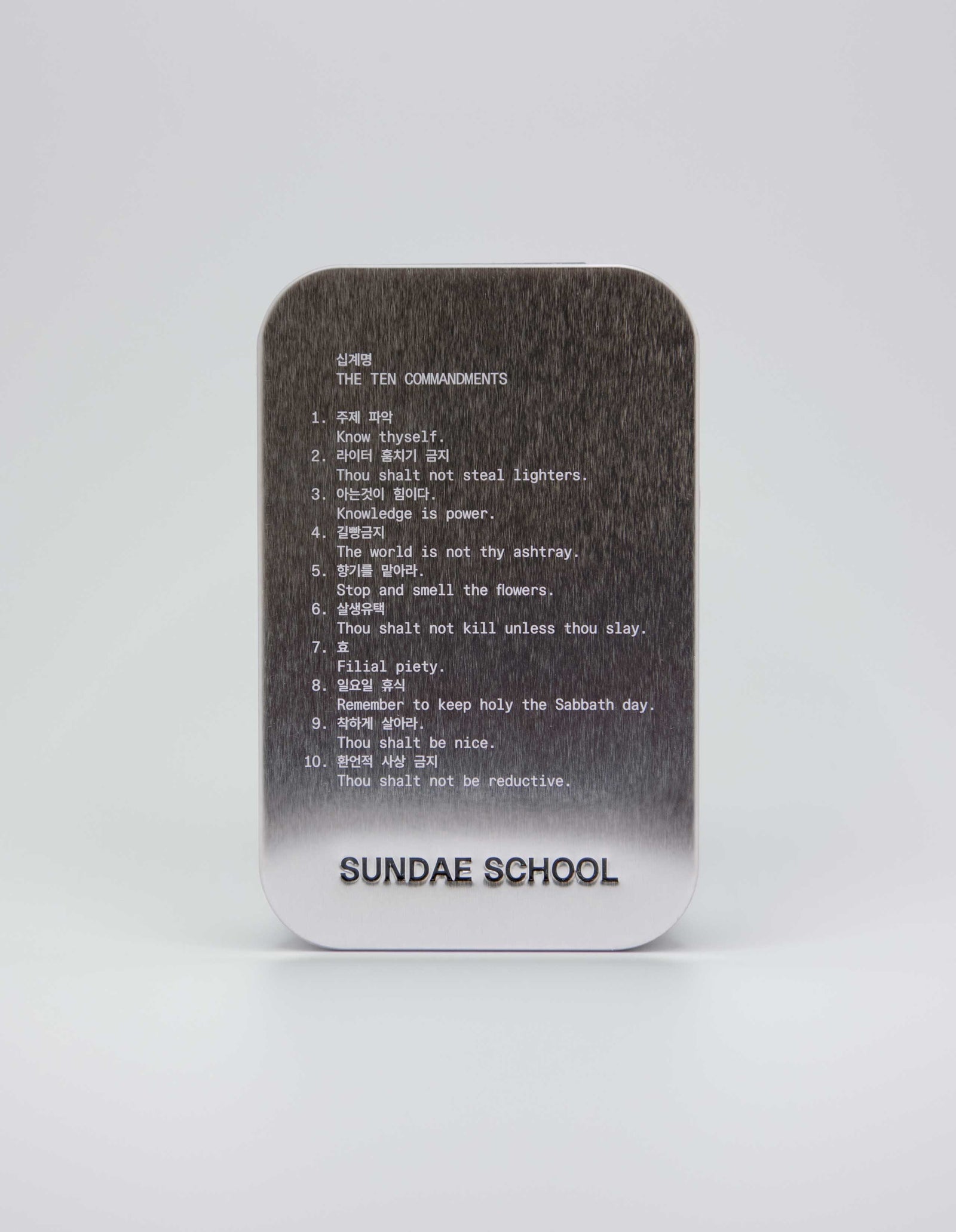 An image of a tin that houses the gummies with the companies 10 commandments:
1. Know Thyself.
2. Thou shalt not steal lighters.
3. Knowledge is power.
4. The world is not thy ashtray.
5. Stop and smell the flowers.
6. Thou shalt not kill unless thou slay.
7. Filial piety.
8. Remember to keep holy the Sabbath day.
9. Thou shalt be nice.
10. Thou shalt not be reductive. 
with a embossment of their company name at the bottom of the tin "Sundae School".