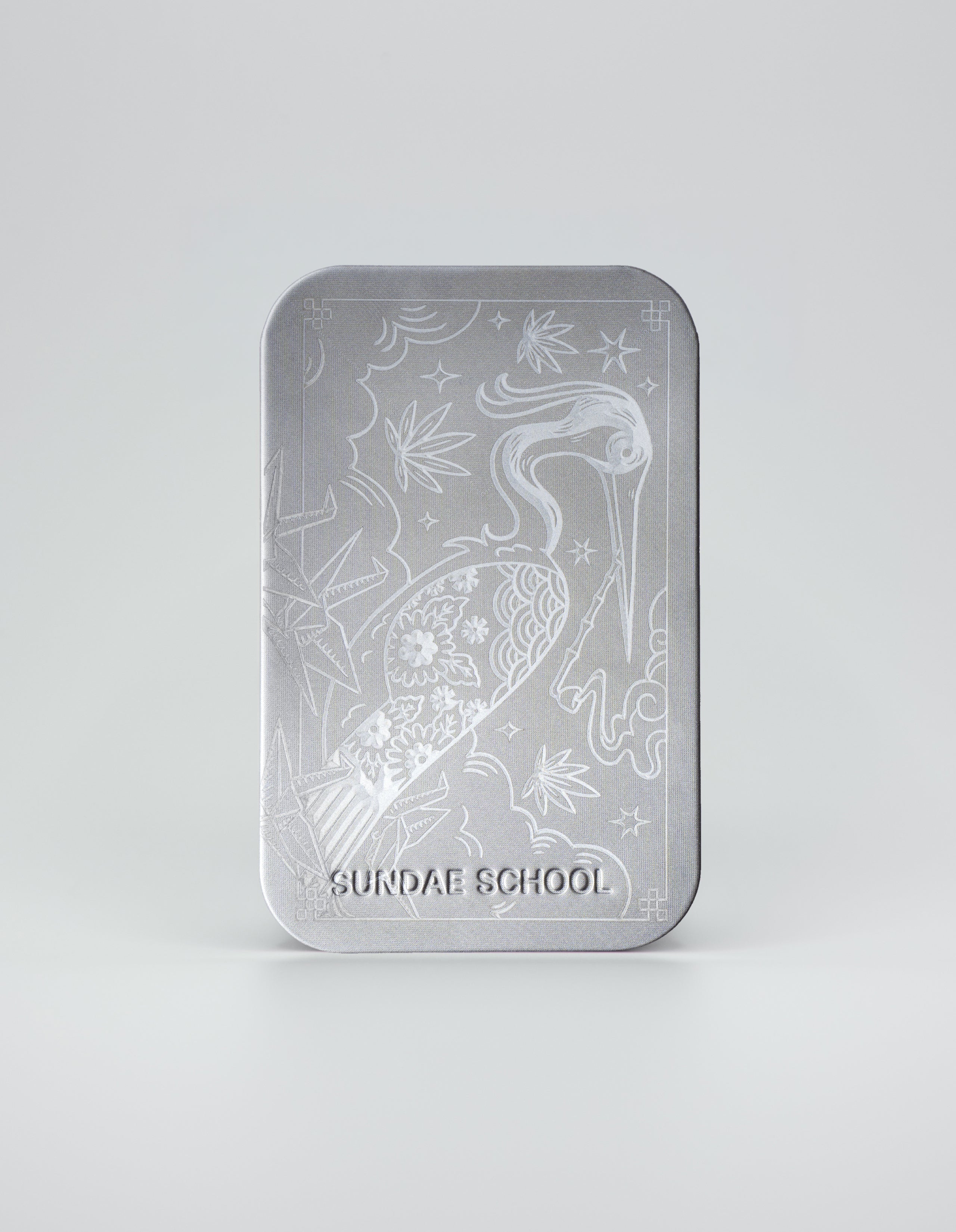 A vertical silver metallic tin featuring an intricate custom-etched illustration of a crane, stylized clouds, stars, and floral patterns. The 