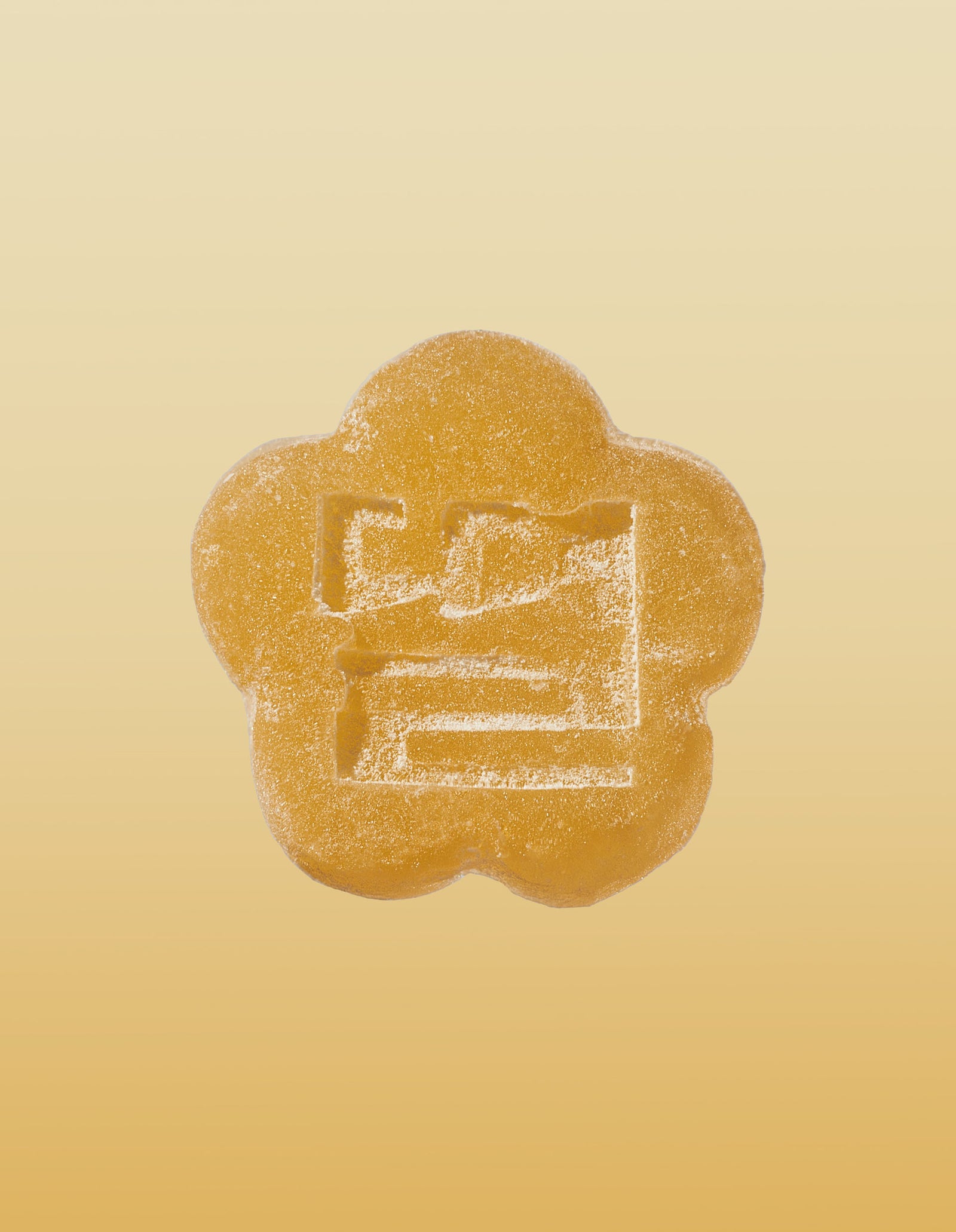An image of a golden pear gummy on a gradient background going light yellow to brownish-orange. 